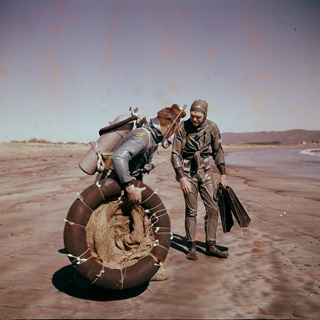 Two unidentified men in diving gear with small, round raft. These diving suits predate the neoprene wetsuit invented by Sc...