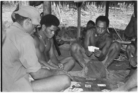 Men playing cards; in middle is Winitaemu.
