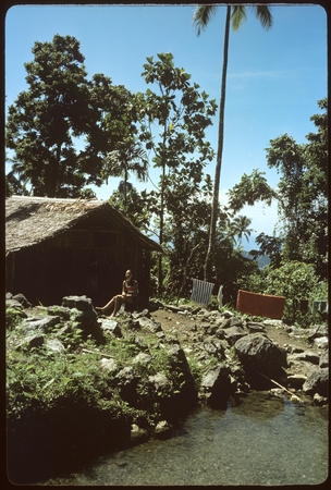 Woman sitting on a rock, in front of building.