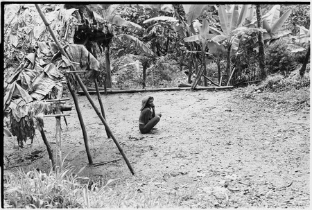 Woman with barkcloth cap sits in a garden clearing, Kumingo