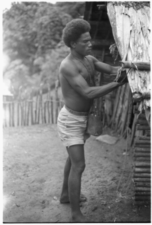 Man hanging shell money on the corner of a house.