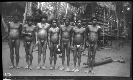 Trobriand men outside yam house; man in center is holding a large gourd, probably for water