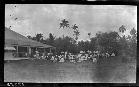 Group of men, women and children sitting in front of building for a hookworm lecture