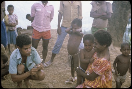 Maternal and child health clinic, health care worker prepares injections, watched by children and parents