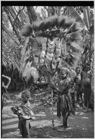 Bride price ritual: man holds large payment banner of feather and shell valuables, marsupial skins