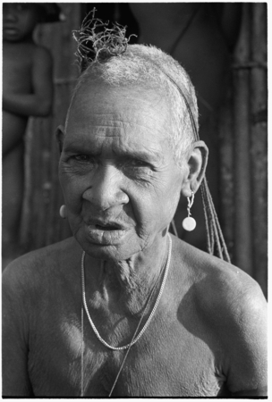 An elderly Kwaio woman, her woven &#39;purse&#39; over her head, wearing shell earrings.