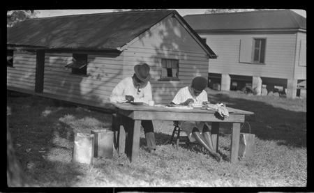 Two men sitting at a table, and buildings in background