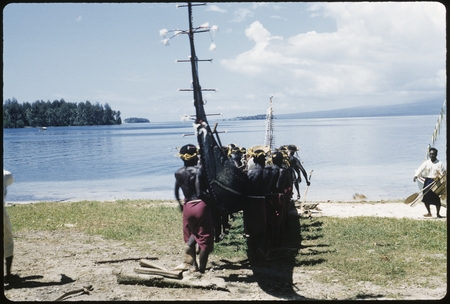 Men carrying canoe to sea; matching red skirt and headress
