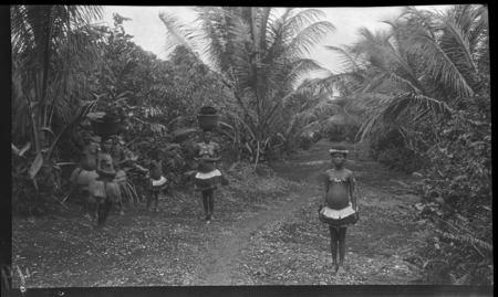 Trobriand women on path, carrying baskets on head
