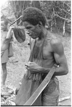 Man standing with bushknife and functional kafa comb in hair.