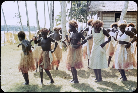 Dancers in grass skirts and matching headress; some with western dress or tops