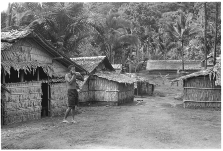 Man blowing a conchshell horn in what appears to be a coastal Christian village, likely not in Kwaio.