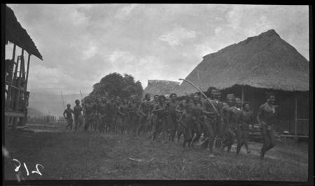 Group of men and boys walking through village, and dancing and singing, at Popole Mission