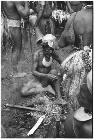 Pig festival, pig sacrifice, Tsembaga: older man sits by fire, surrounded by decorated men