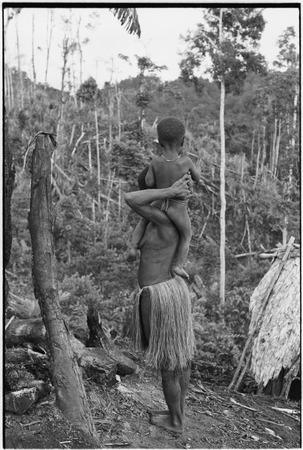 Yeria, Wanuma Census Division: woman with grass skirt carries small child near garden