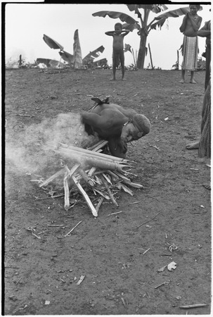 Pig festival, stake-planting, Tuguma: Tsembaga man heats bamboo which will explode, signaling time to leave for Tuguma