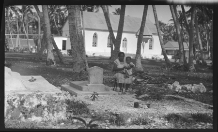 Cook Islands woman and infant in a cemetery, church in background