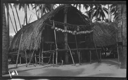 House with pole of coconuts and pole of yams hanging, probably in Chiria (Tsiria) village, Yule Island, Central Province