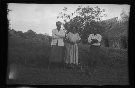 Three Fijian people in front of a traditional house