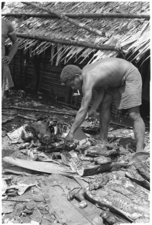 Man with pig head on pile; the head is sacred.