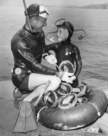 Father and son in diving suits posing with catch of abalone