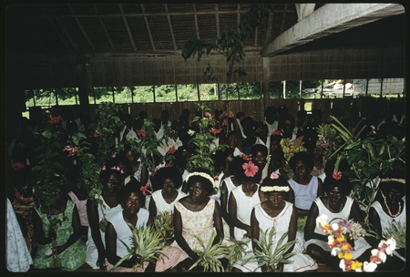 Group of women in a building: seated, holding plants, and flowers in hair