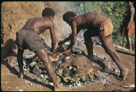 Two men laying pork out on the stone oven.