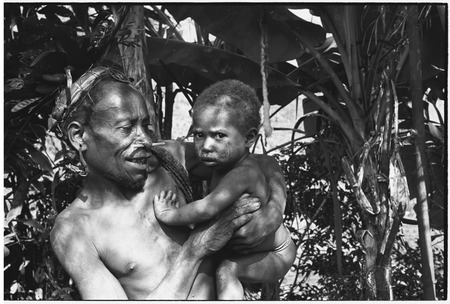 Pig festival, wig ritual, Tsembaga: man with wig frame lashed to his hair, he holds an infant