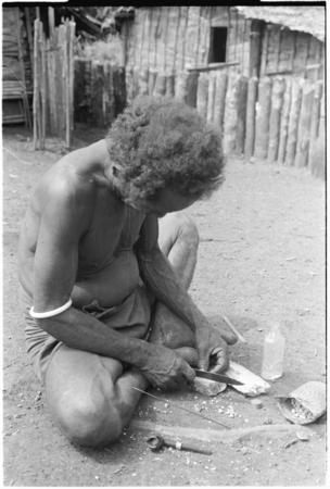 &#39;Iika chipping edges off of coneshells with a knife, one step in making kofu shell money beads, at Fanuaba&#39;ita.