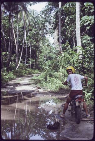 Edwin Hutchins rides his motorcycle on the road to Wawela village