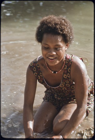 Young woman named Linette, wearing shell necklace and dress, bathes in shallow water