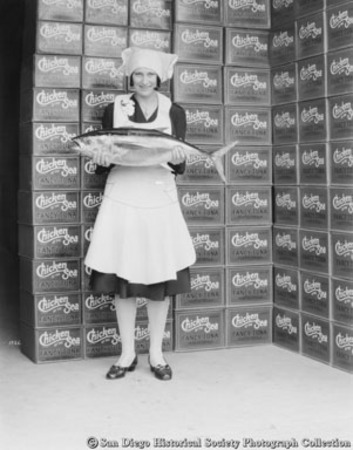 Woman with tuna standing in front of boxes of Chicken of the Sea brand tuna at Van Camp Sea Food Company