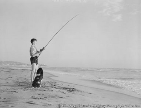 Young man with dog on beach surf fishing