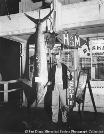 Man with fishing rod posing with swordfish [caught from H &amp; M Sport Fishing Company boat Mascot III?]