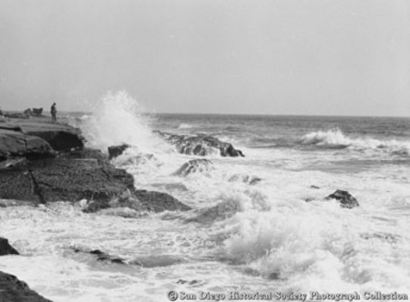 Man overlooking ocean waves crashing on to rocky coast