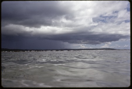 Rainstorm over a low island seen across expanse of water