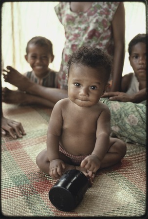 Infant on woven mat plays with canister