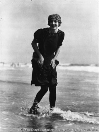 Woman in bathing suit wading in ocean surf on San Diego beach