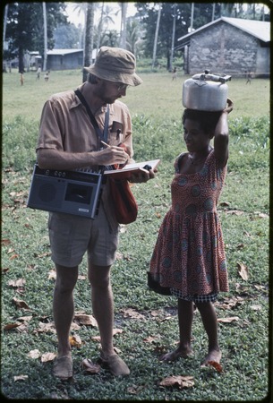 Anthropologist Edwin Hutchins uses tape recorder and takes notes while talking with woman, she carries kettle on her head