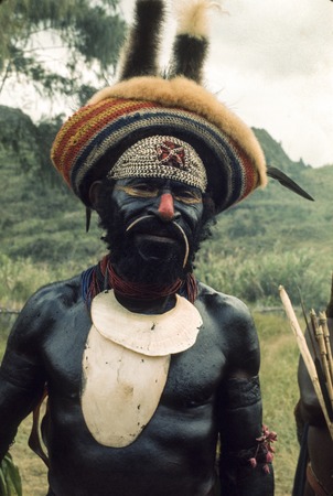 An aging village leader, skin blackened with soot and oil and decorated for ceremonial parading