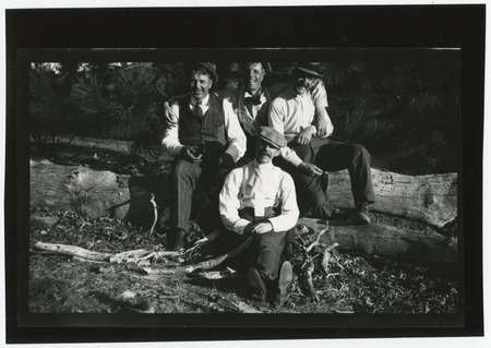 Four men seated on fallen log