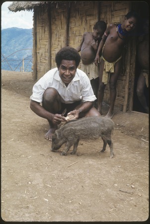 David Gwore feeds his small pig, while children look on