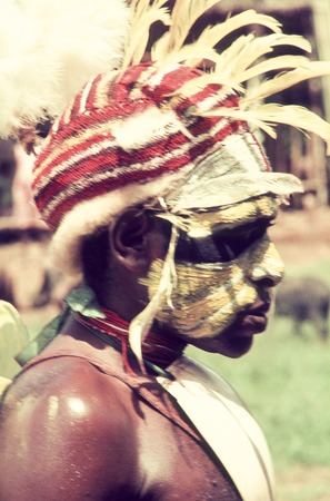 Young man wears face paint, baler shell valuable, red headdress decorated with yellow cockatoo feathers and marsupial fur