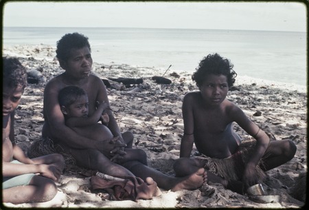 Woman and children sit on a beach near Kaibola village