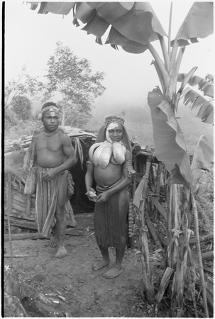 Bride price ritual: man stands beside a smiling woman adorned with large shell valuables, part of her bride price