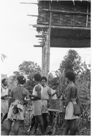 Men standing under raised house at feast.