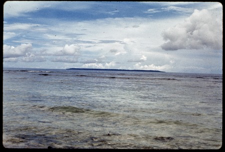 Island in the distance across lagoon, waves breaking on reef