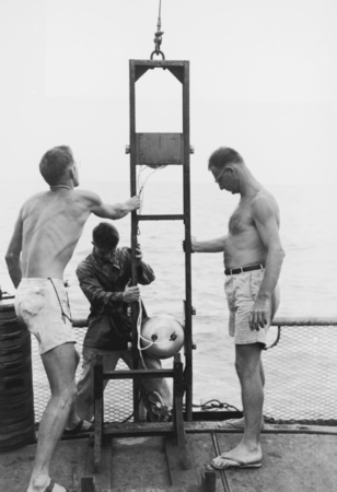 Walter H. Munk (right) and two men lower camera into the water near Palmerston Island