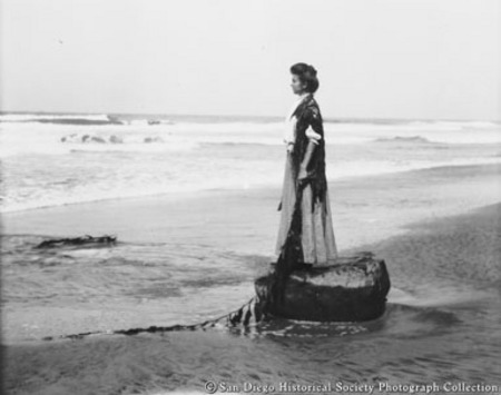 Marion Davis, draped in kelp, standing on beach looking at ocean, Encinitas