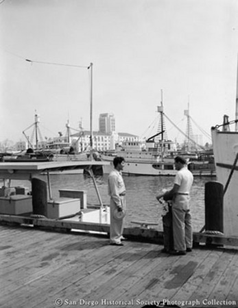 General view of San Diego waterfront showing docked tuna boats and two men on wharf